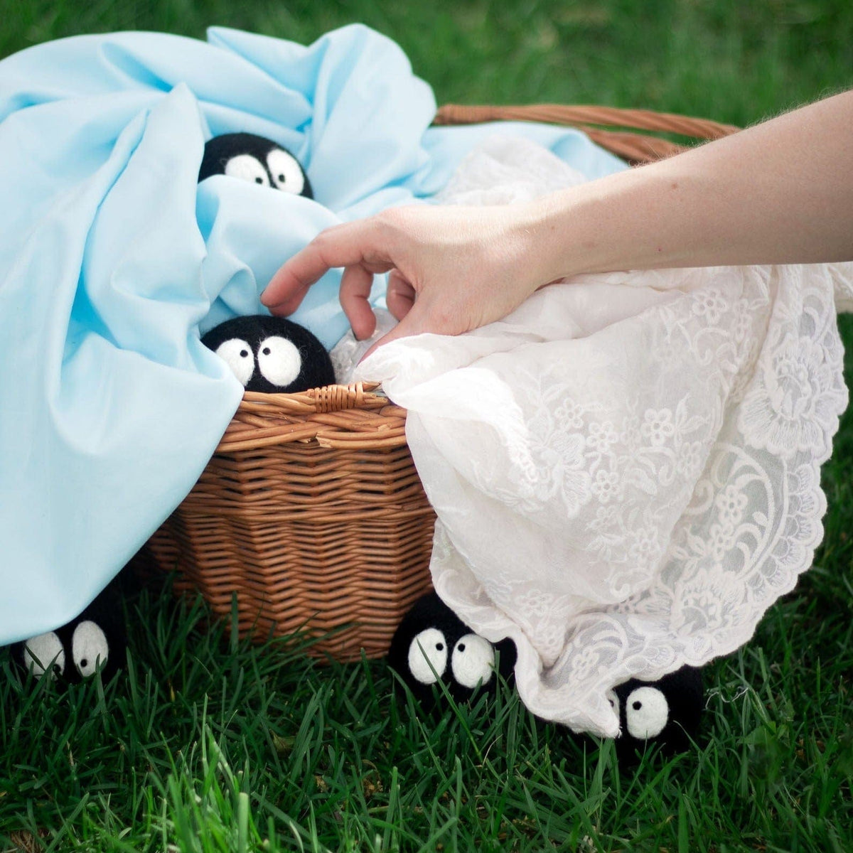 Person lifting plush black sheep-faced laundry dryer balls from a wicker basket