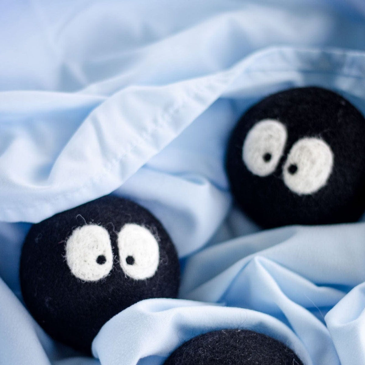 Three plush black sheep-faced laundry dryer balls on light blue fabric