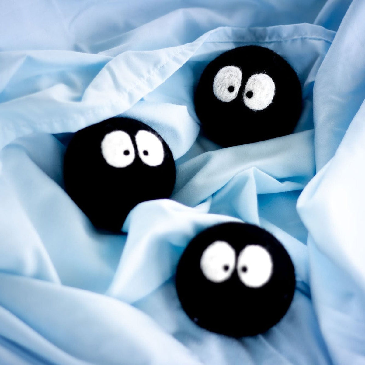 Three black plush balls with white cartoon eyes nestled in light blue fabric
