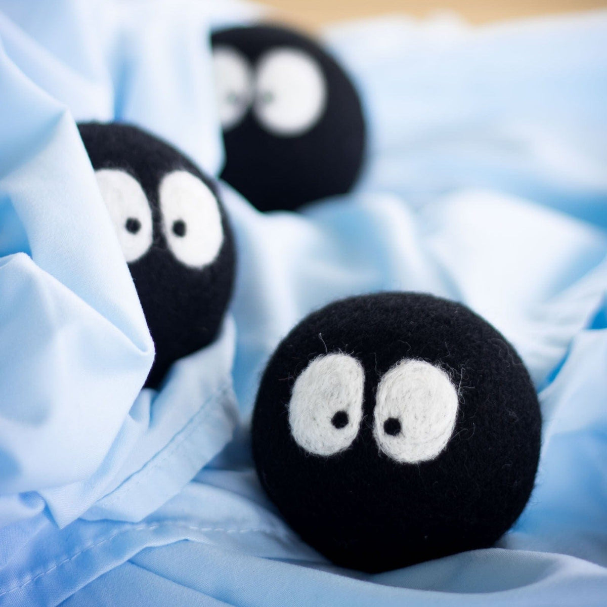 Black plush laundry balls with white eyes on light blue fabric, one near center