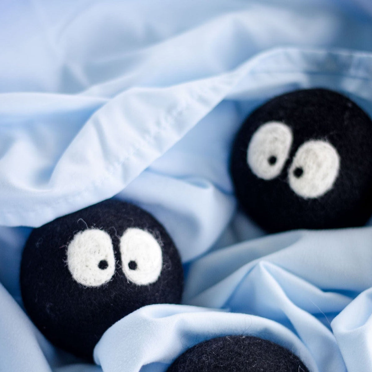 Three black plush laundry balls with white eyes partially covered by light blue fabric