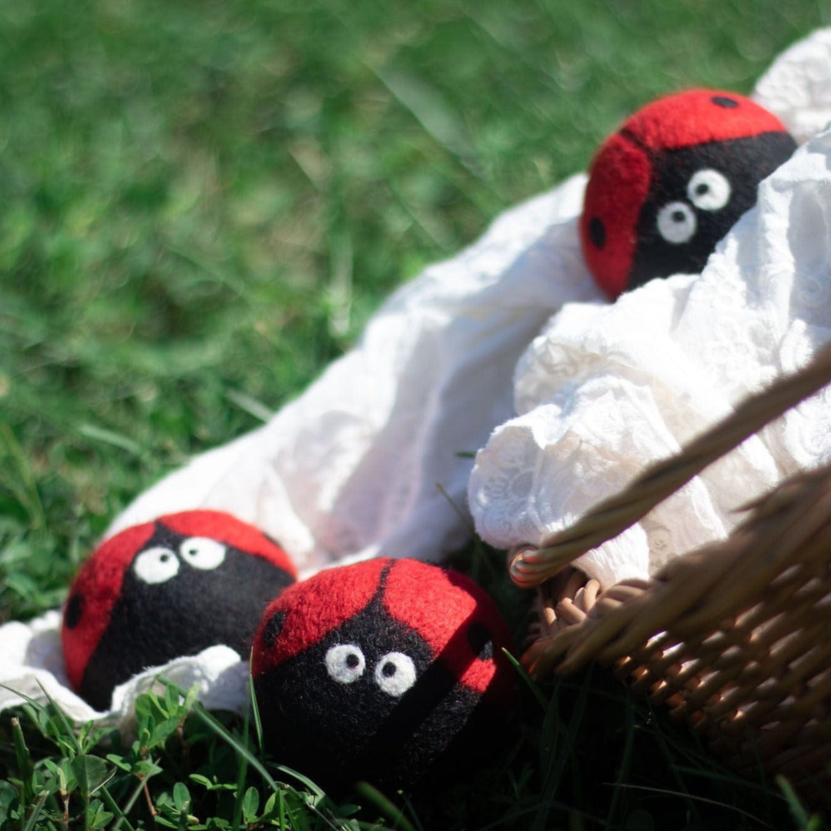 Plush ladybug dryer balls on grass beside a white cloth, red-and-black with eyes