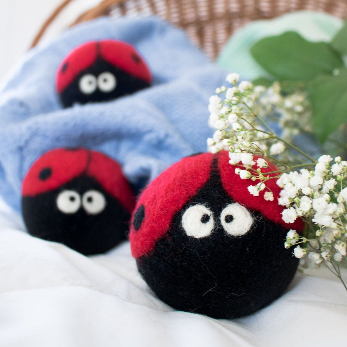 Set of plush ladybug dryer balls on white fabric, red tops and black bodies