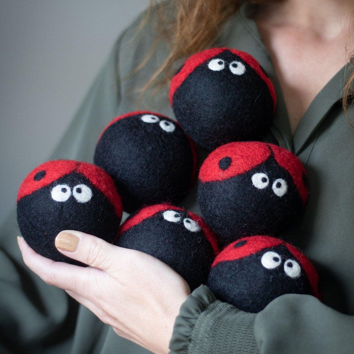 Hand holding plush ladybug dryer balls, red-and-black bodies with white eyes