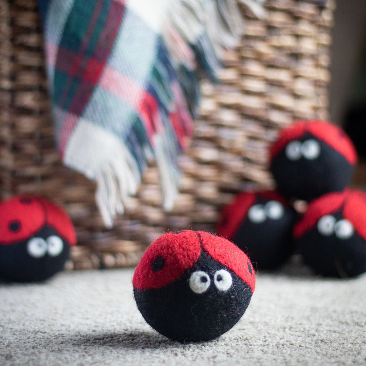 Ladybug dryer balls on a rug near wicker and plaid fabric, red-and-black plush
