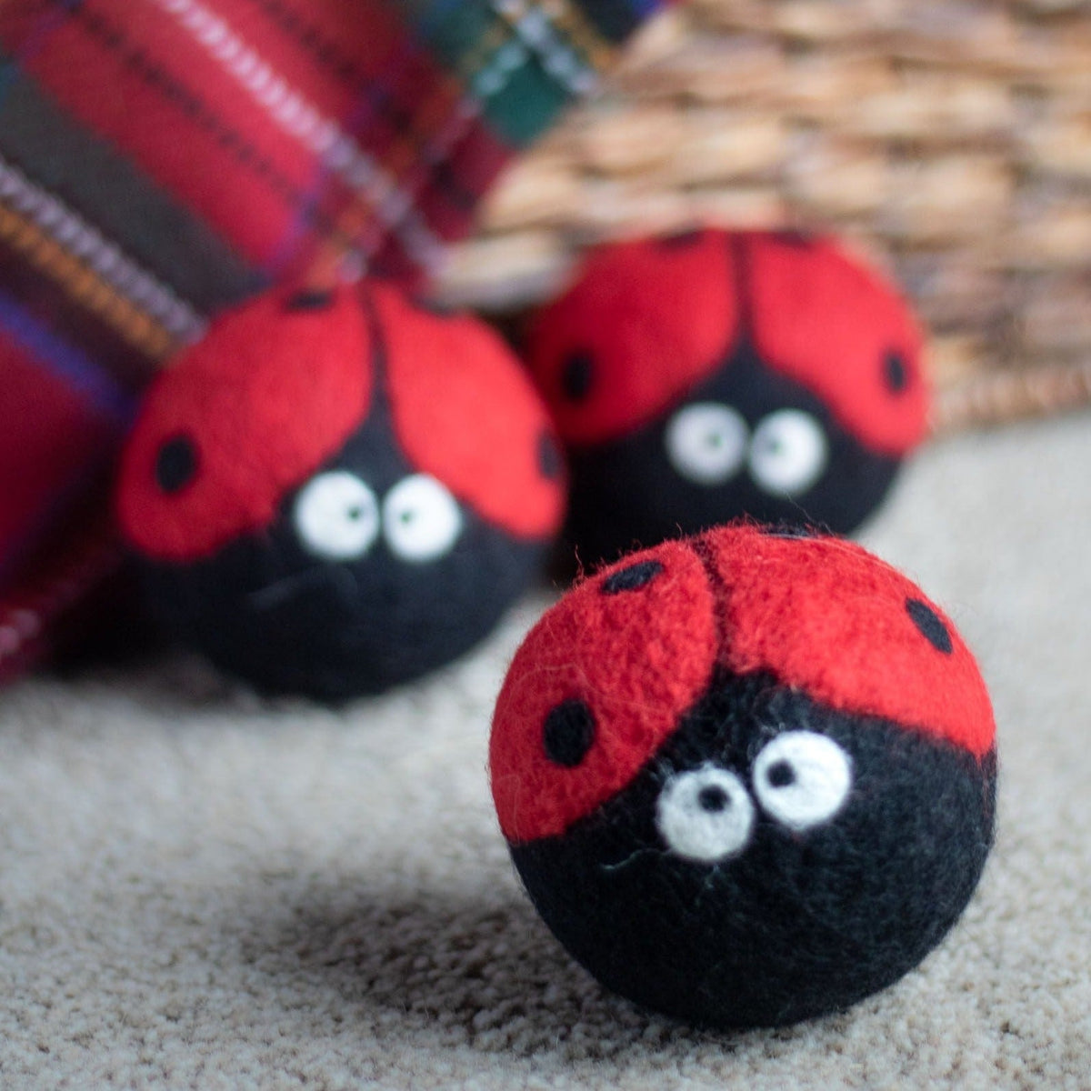 Close-up of plush ladybug dryer balls on light fabric, red-and-black with eyes