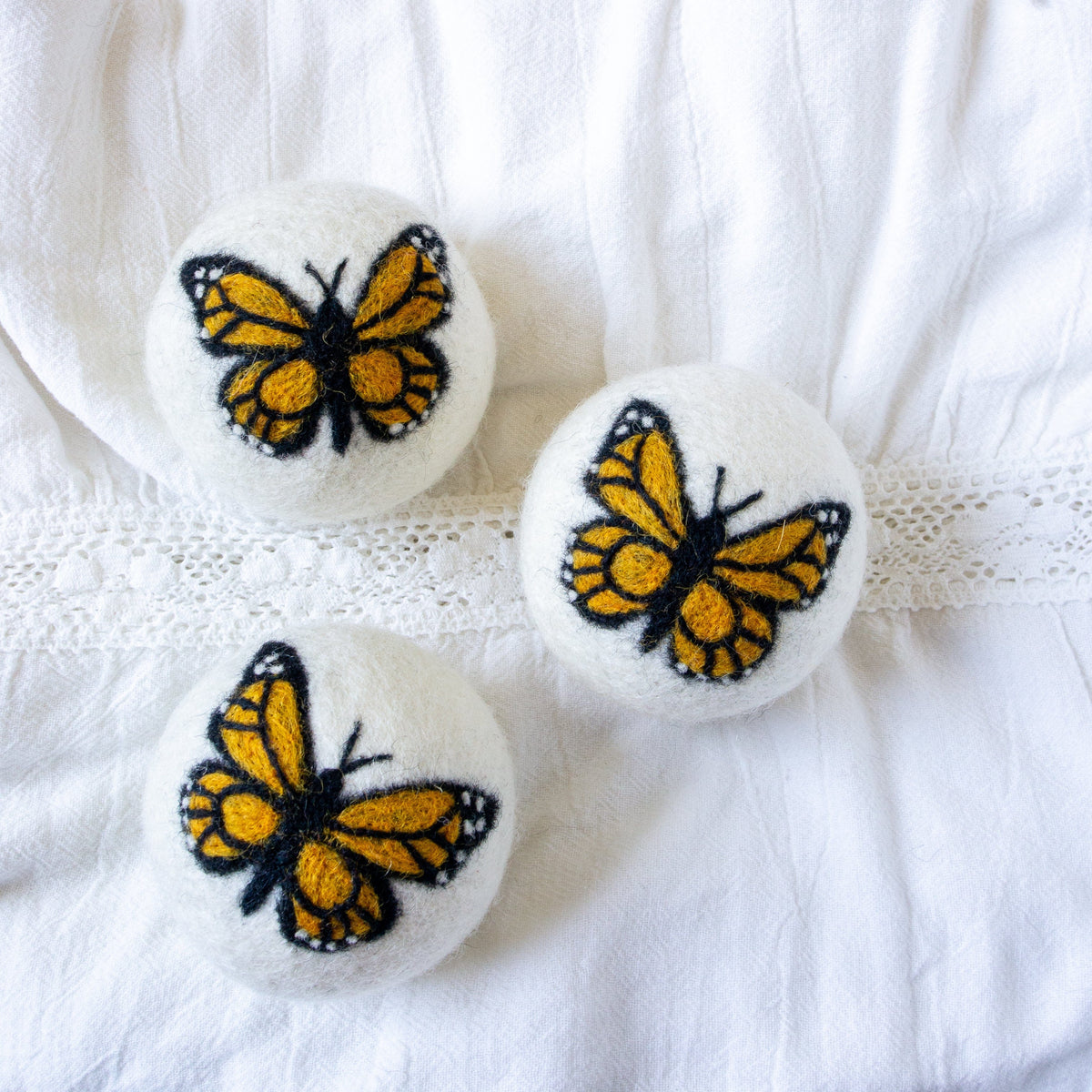 Three Monarch butterfly embroidered felt balls on white fabric