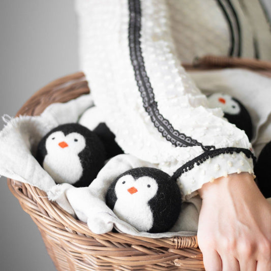 Three penguin plush toys in a woven basket lined with white fabric