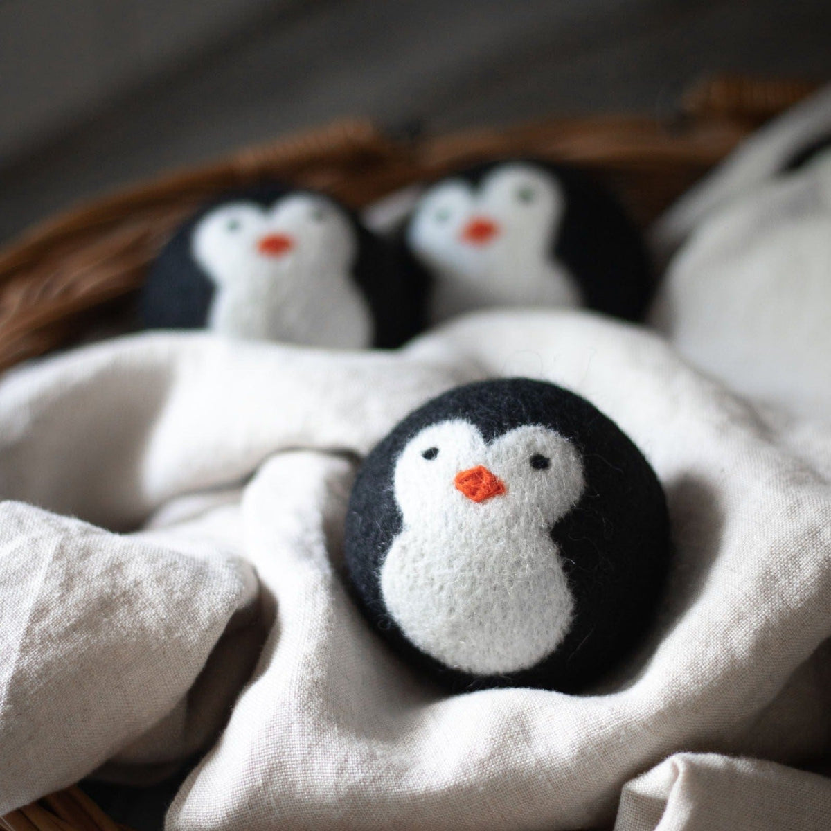 Penguin plush trio resting on light fabric, featuring one close-up penguin
