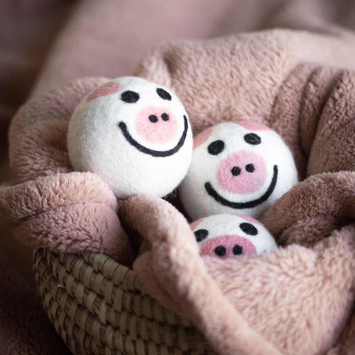 Four pig plush toys nestled in a fluffy taupe blanket
