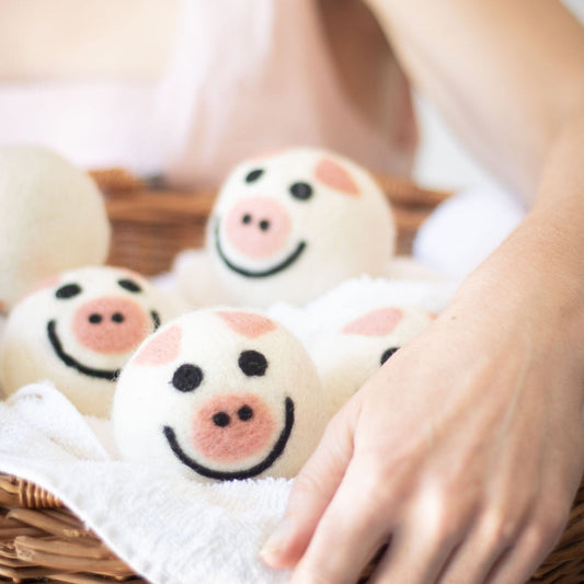 Hand placing a small pig plush on a soft blanket with other pig plush toys