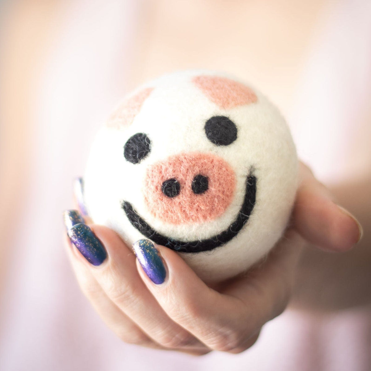 Single round pig plush toy with embroidered smile and pink snout in a hand