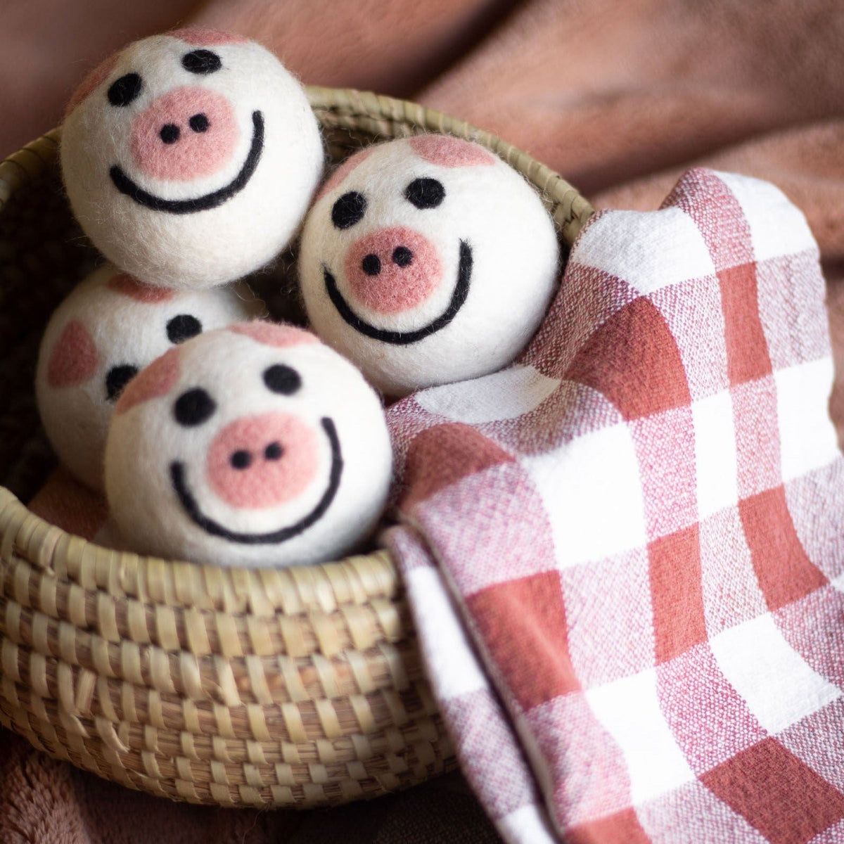 Felt pig dryer balls in a basket with a pink-and-white checkered cloth