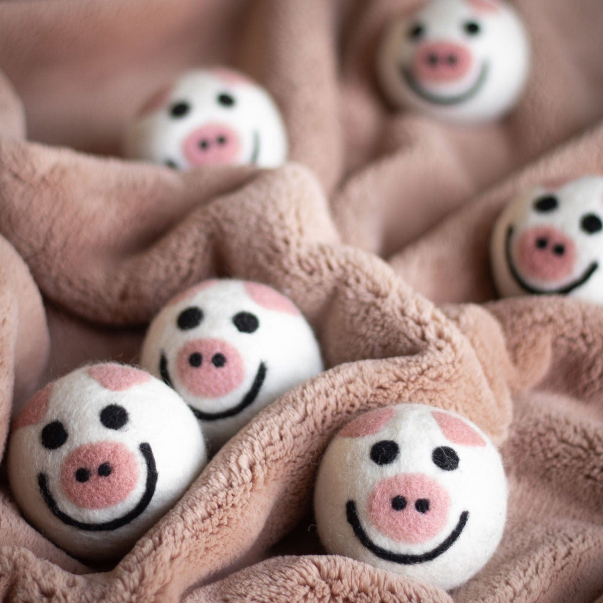 Felt pig-shaped dryer balls on a soft brown fabric surface