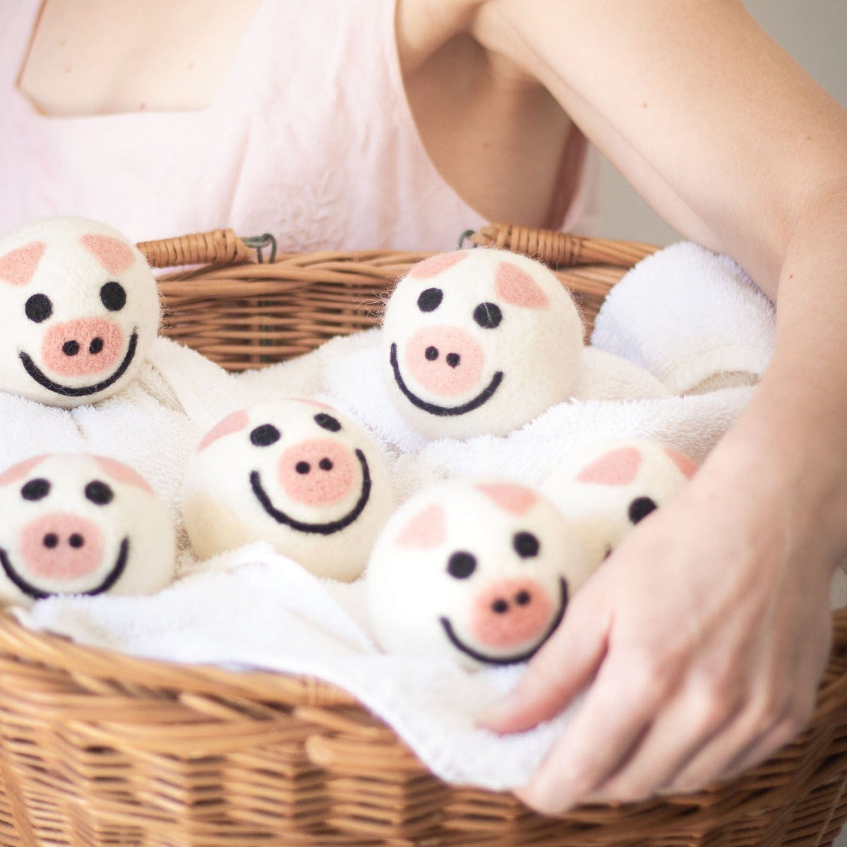 Felt pig-shaped dryer balls in a woven basket, with hands reaching in