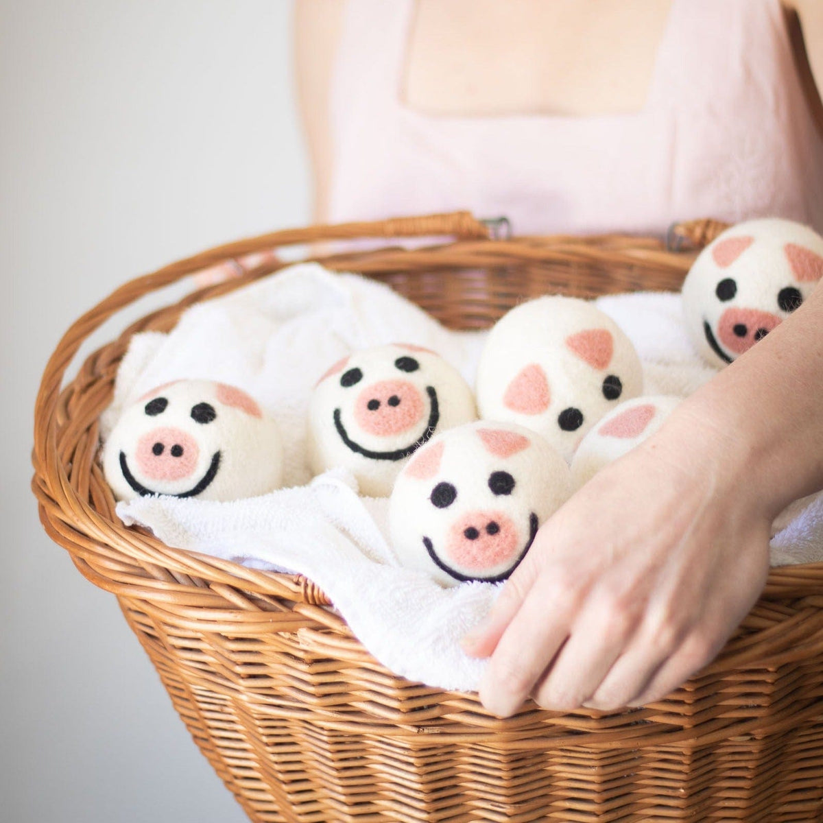 Felt pig-shaped dryer balls in a woven basket, held by a hand