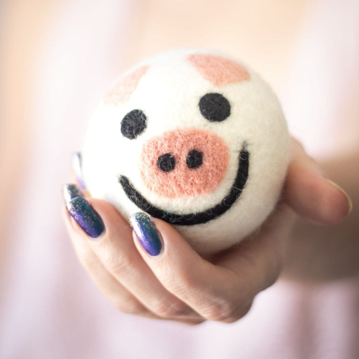 Single felt pig-shaped dryer ball with smiling face and rosy cheeks