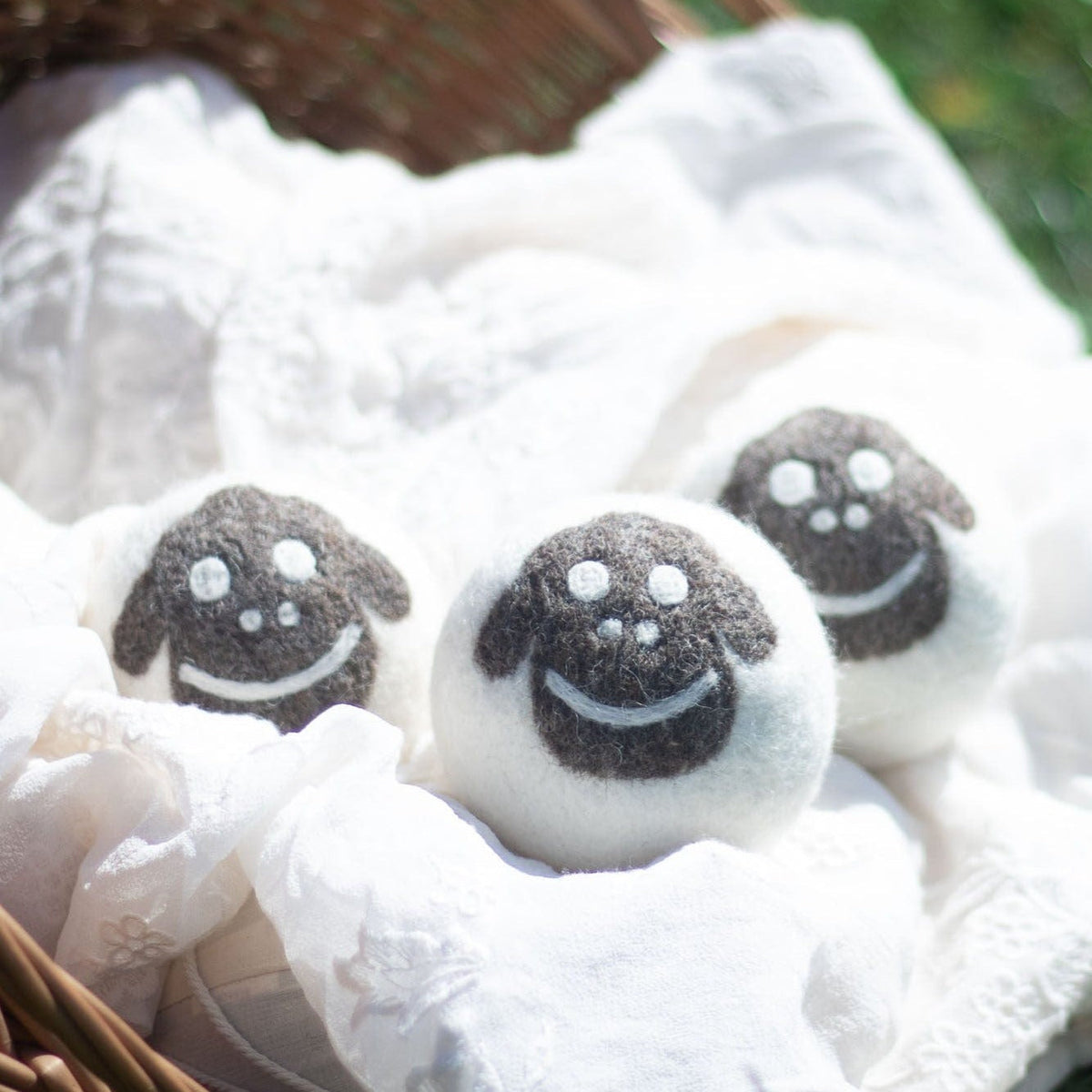 Three felt sheep plush balls with embroidered smiles on white cloth