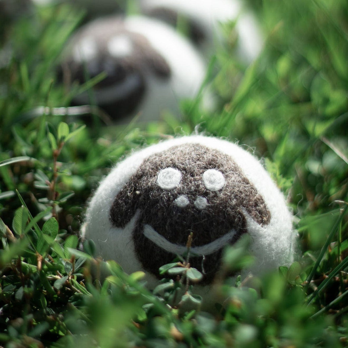Single felt sheep plush ball with embroidered smile on grass