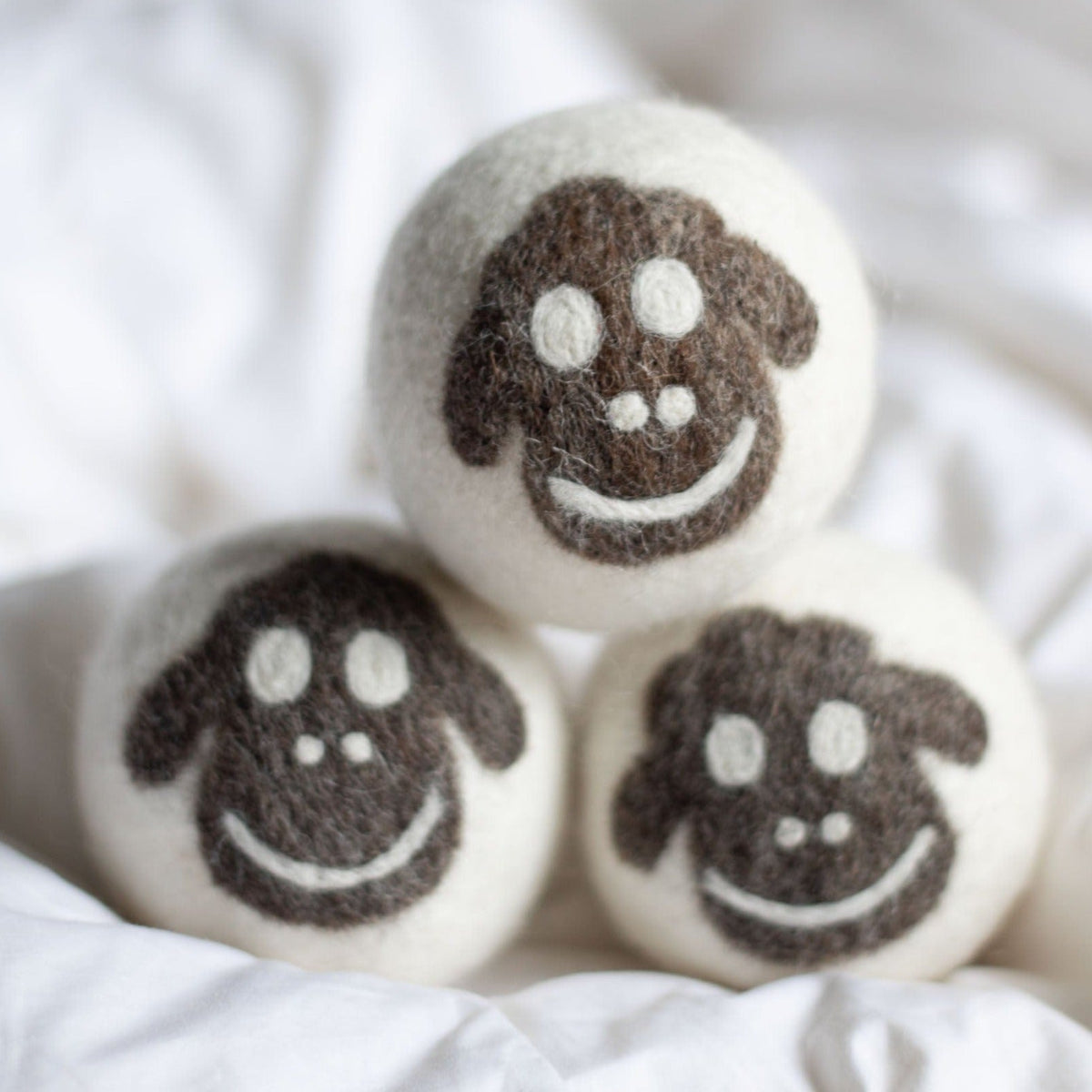Felt sheep plush trio, three smiling faces on white fabric