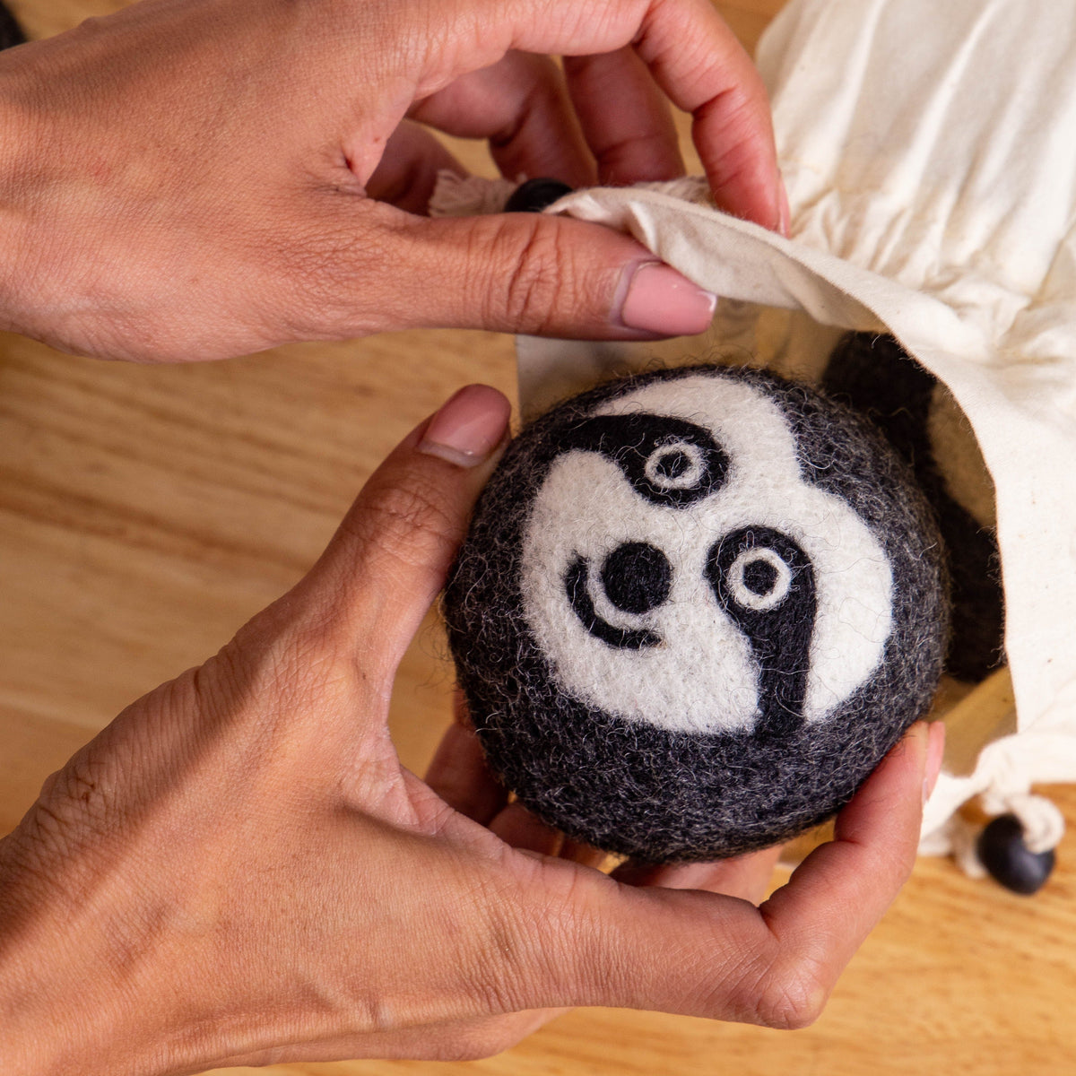 Felt sloth dryer ball with embroidered face being placed in a paper box