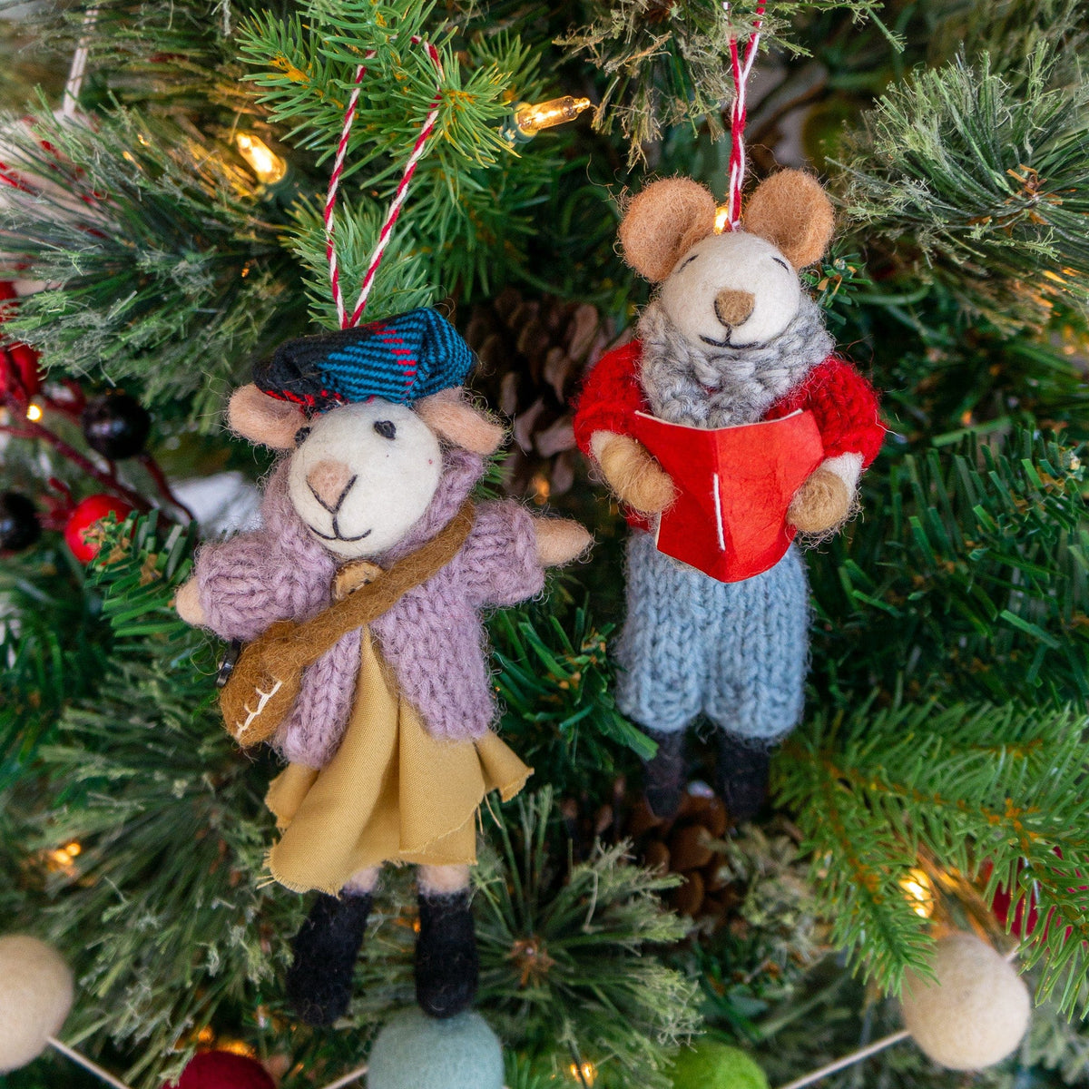 Two boho felt mouse ornaments hanging on evergreen: guitar outfit and red gift outfit