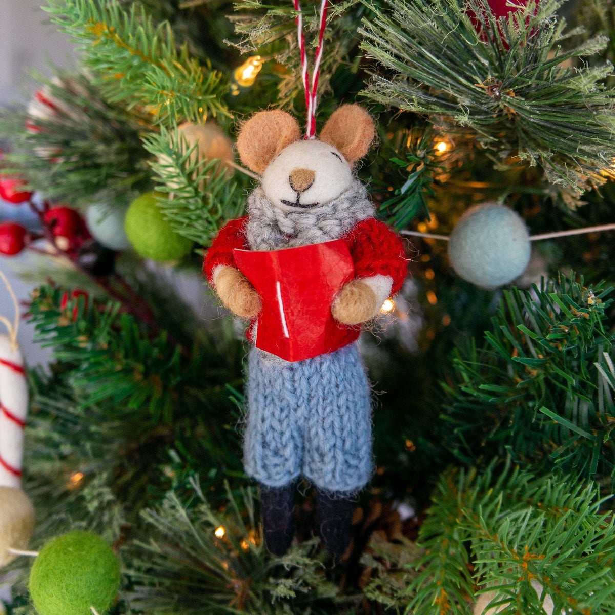 Hanging felt mouse ornament in a red vest and blue knit pants on a Christmas tree