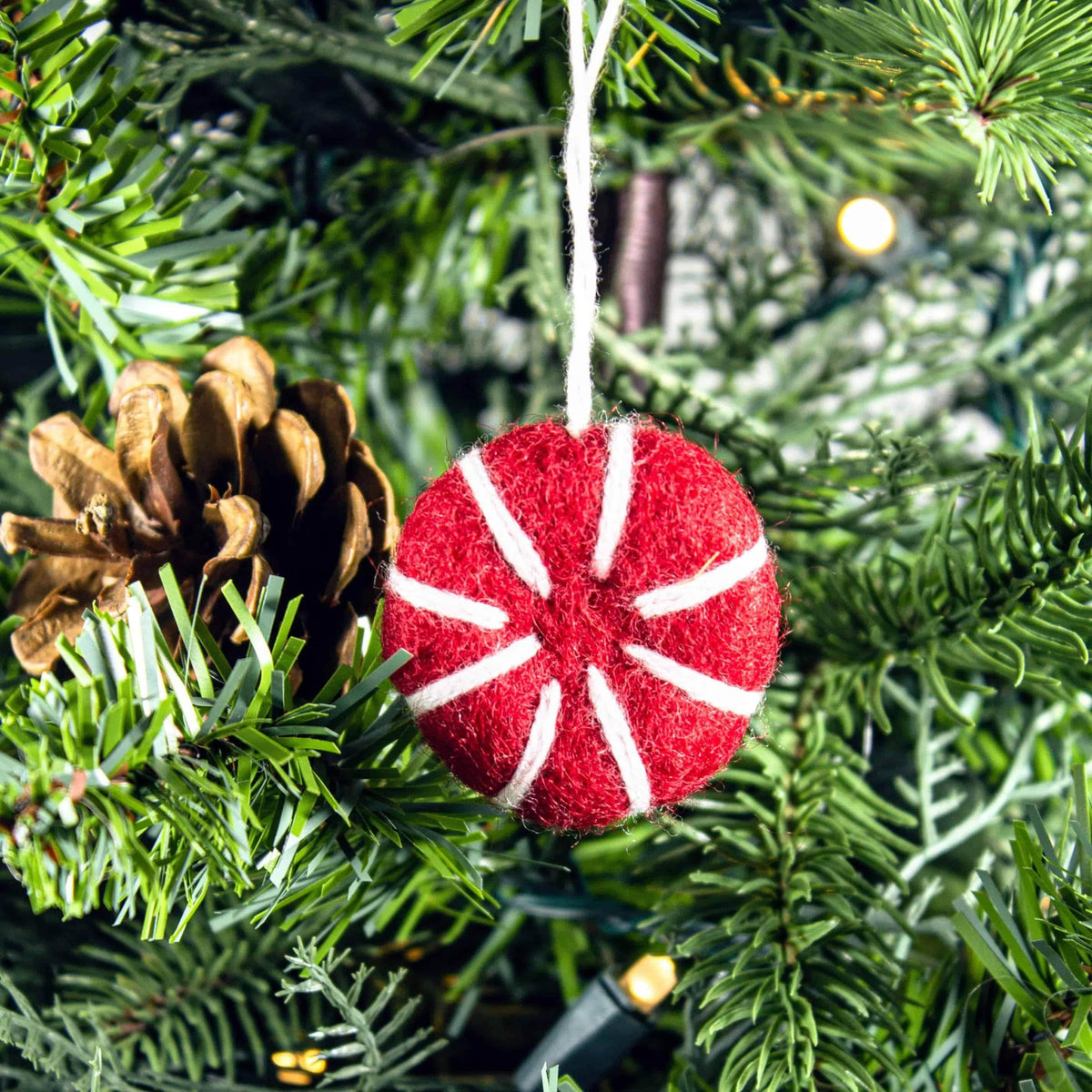 Red-and-white felt peppermint ornament freshener hanging on pine branches