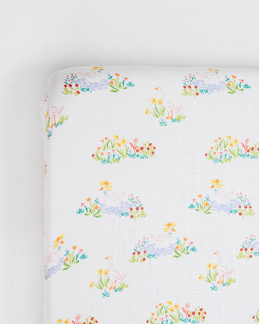 White crib sheet with colorful garden animal and flower pattern.