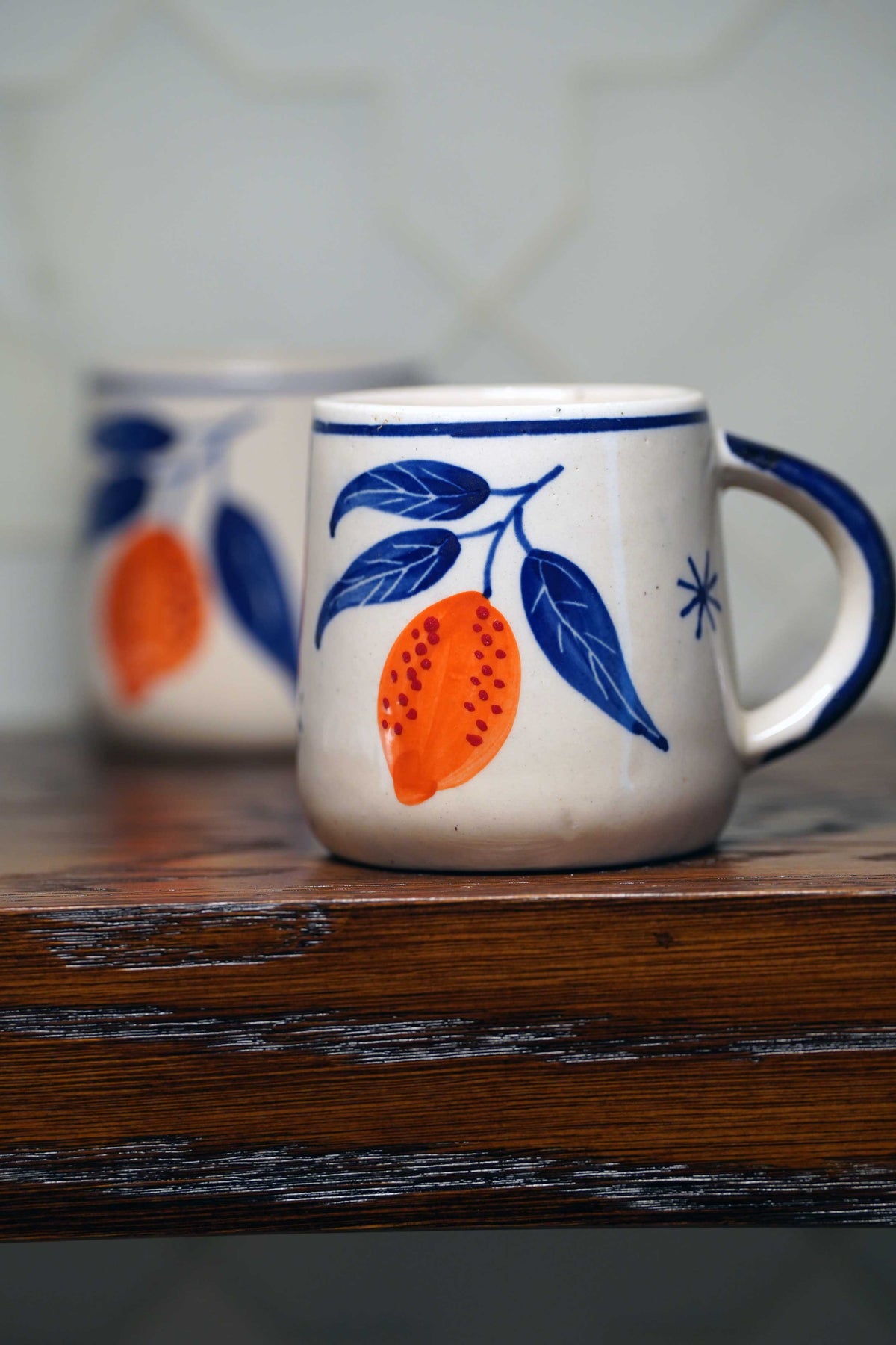Ceramic coffee mug with white base and blue rim, featuring orange lemon illustration