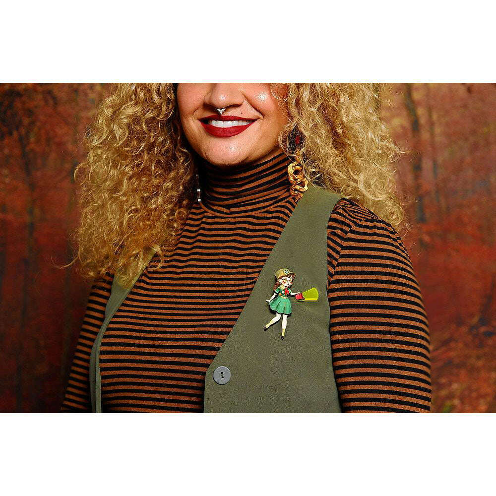 Girl Scout brooch pinned on dark green clothing with a striped top