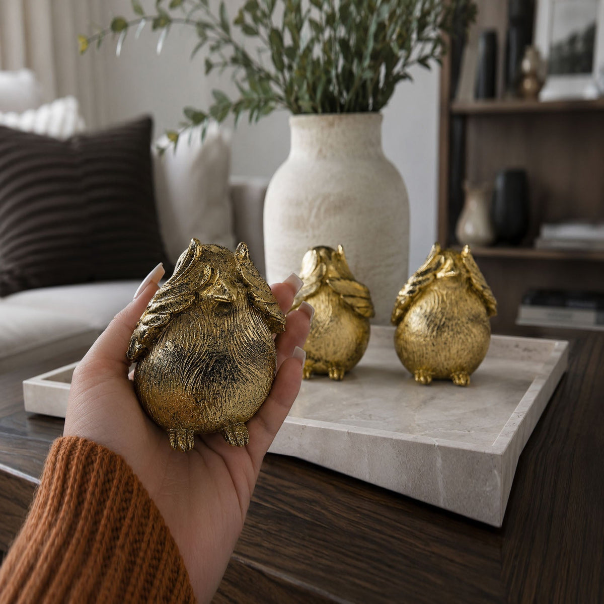 Gold-tone bird figurine held in hand, with two matching birds on a stone tray