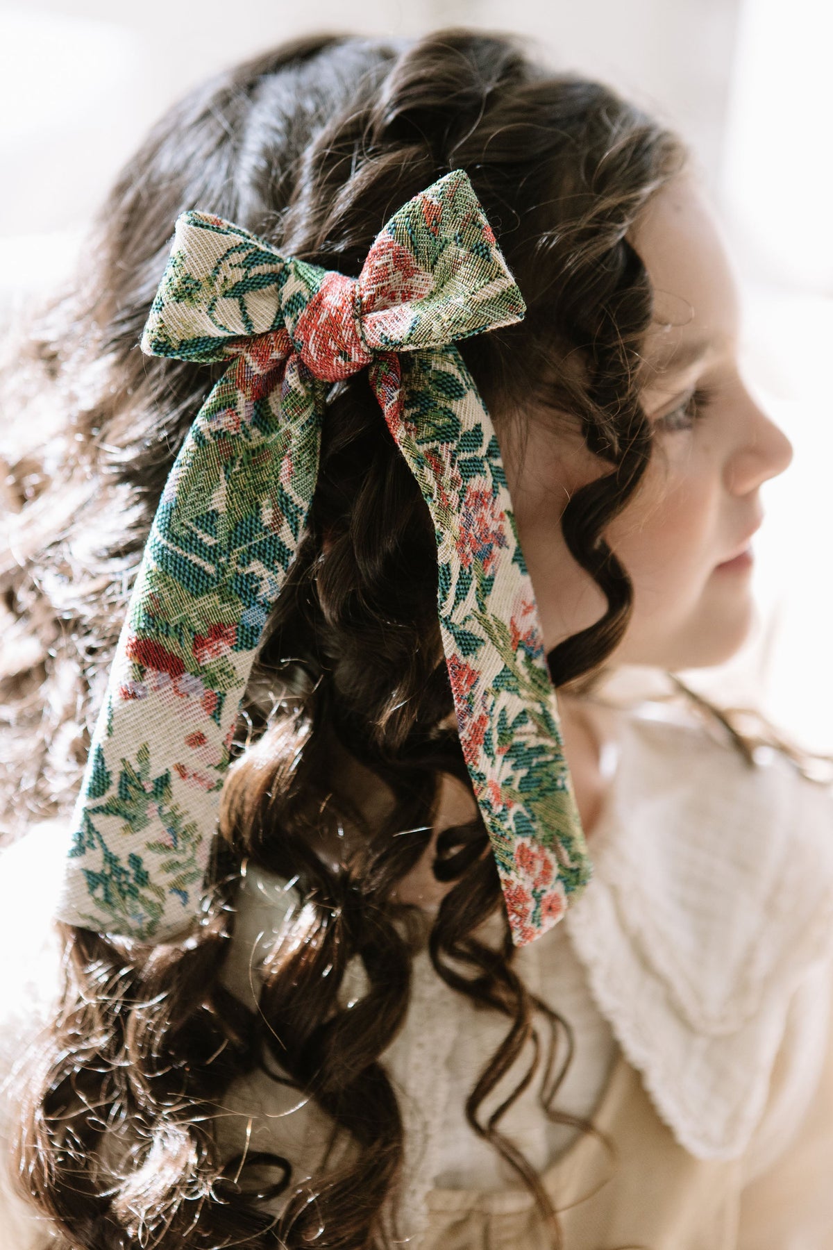 Floral plaid hair bow tied on dark curly hair, with long ribbon ends