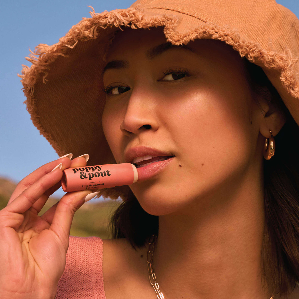 Pink grapefruit lip balm tube held to lips on a model
