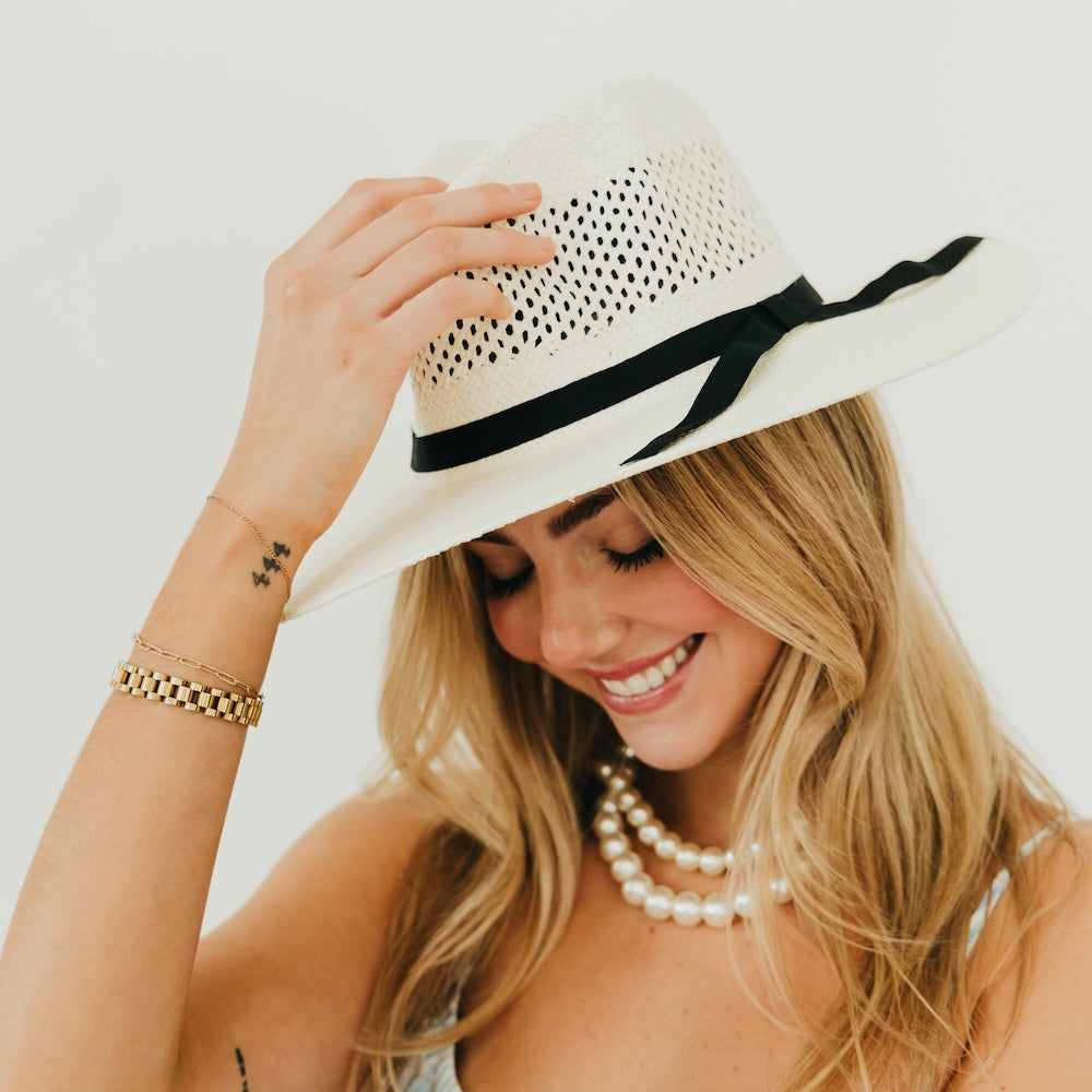White perforated western sun hat with black band and ribbon tails, wide brim.