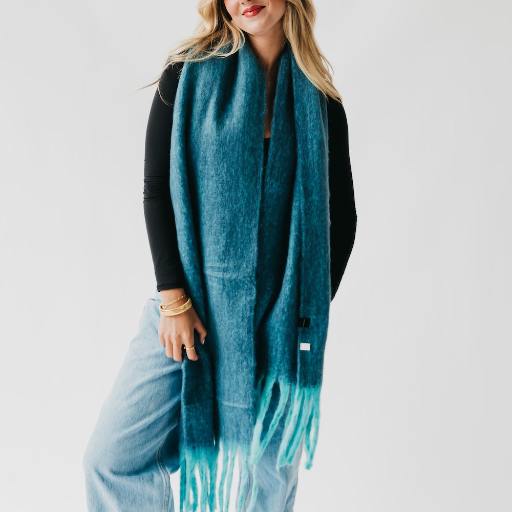 Teal blanket scarf with tassel fringe, layered over light blue jeans