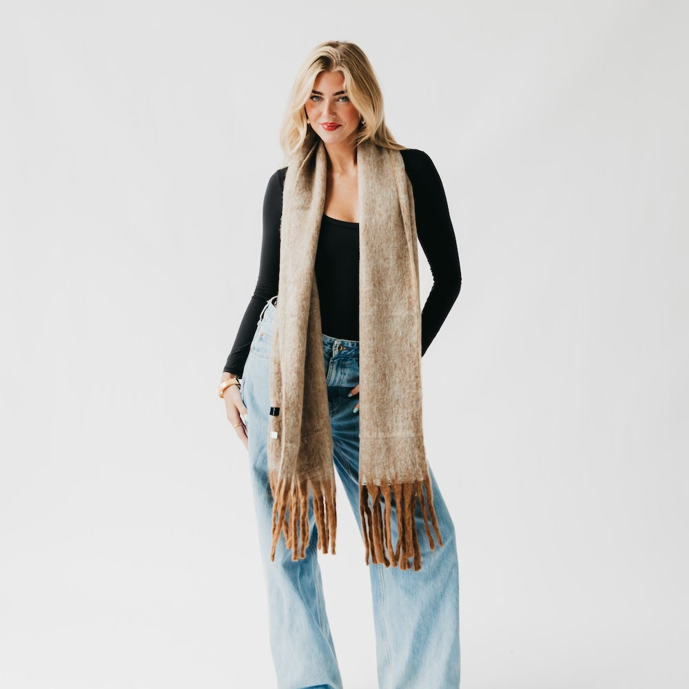 Tan blanket scarf with long fringe, draped down over a black top