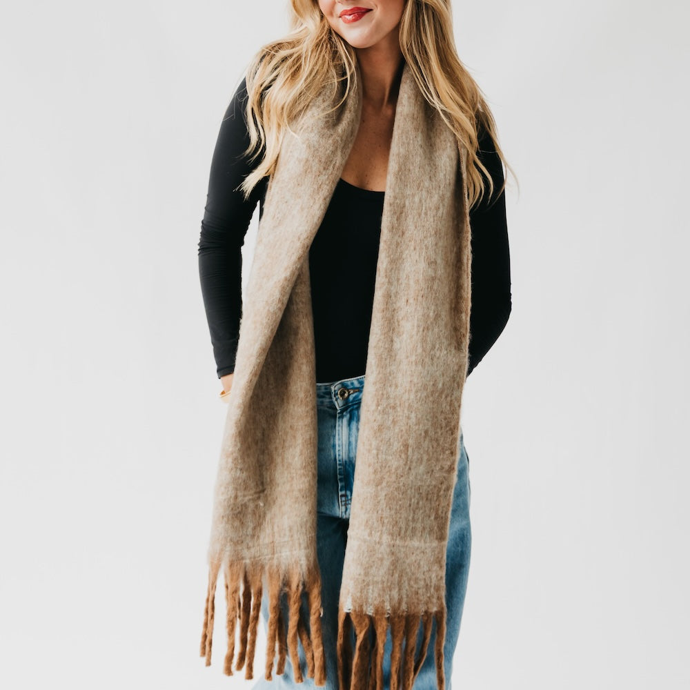 Tan blanket scarf with long fringe, draped over a black top