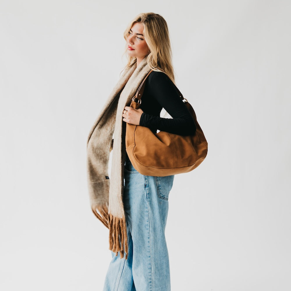 Tan blanket scarf with fringed ends, worn with a brown shoulder bag