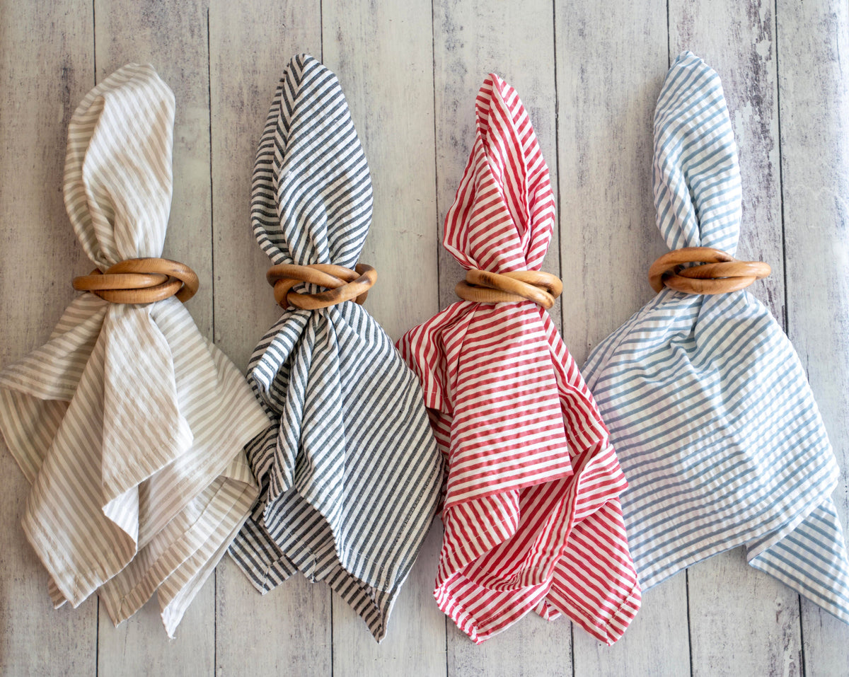 Wood napkin rings on folded striped and solid cloth napkins, four tan rings