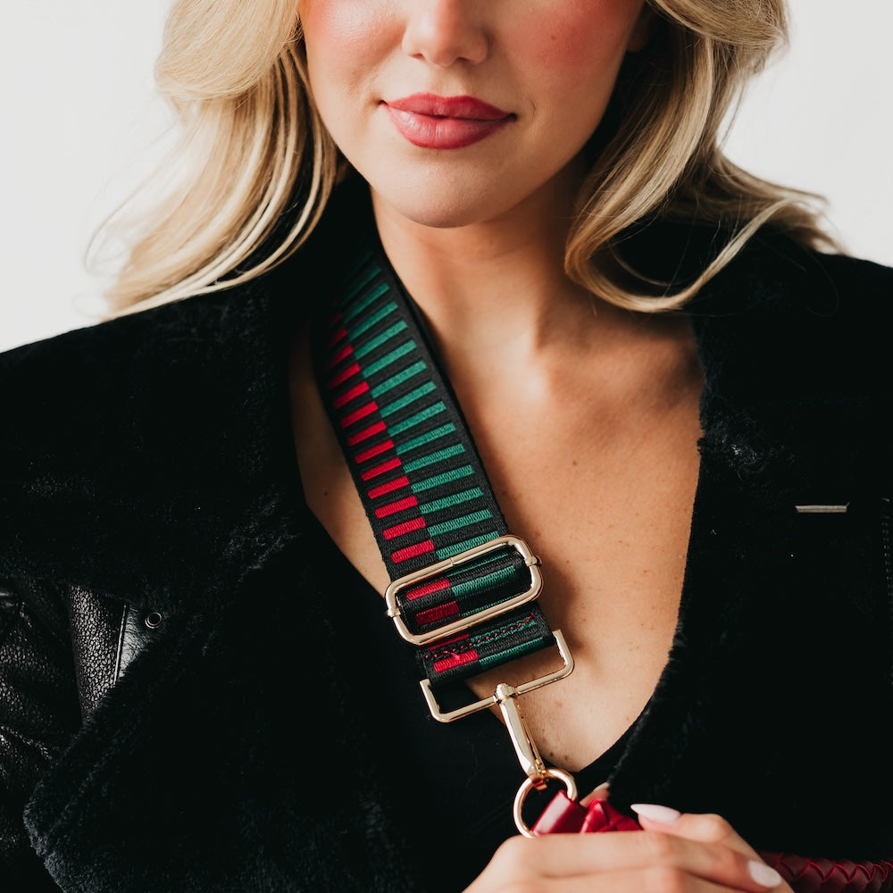 Adjustable bag strap with striped green, black, and red webbing and gold buckles
