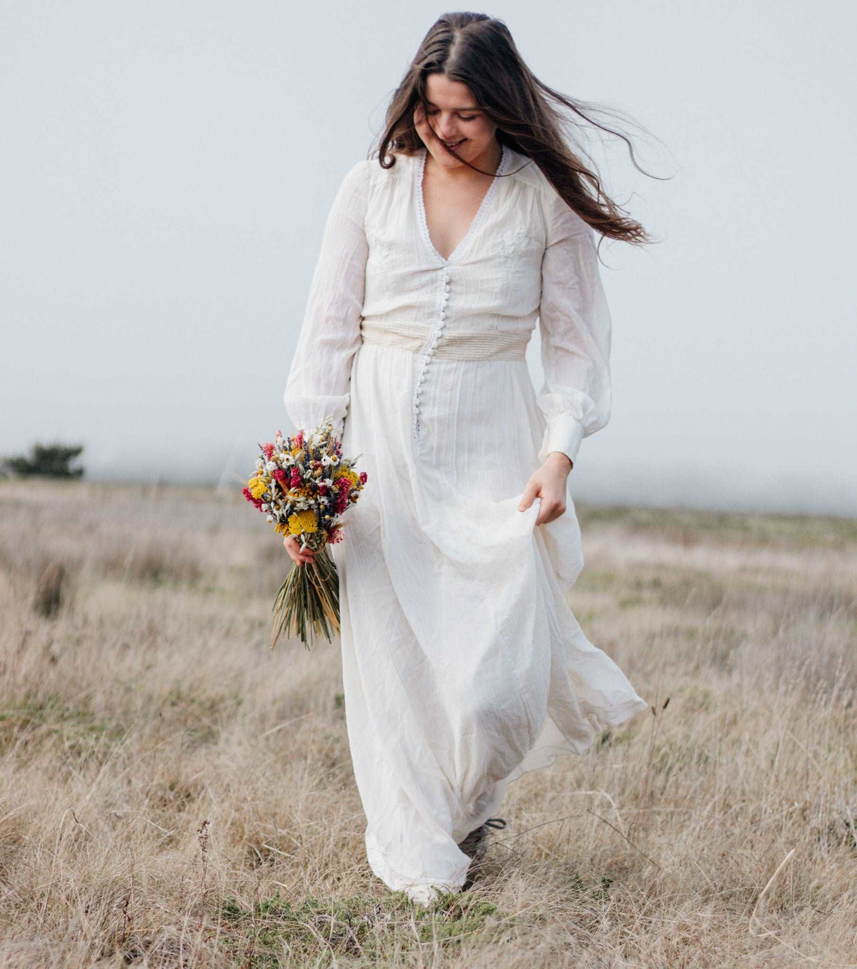 Woman carrying dried flower bouquet in a white dress, bouquet held by long stems