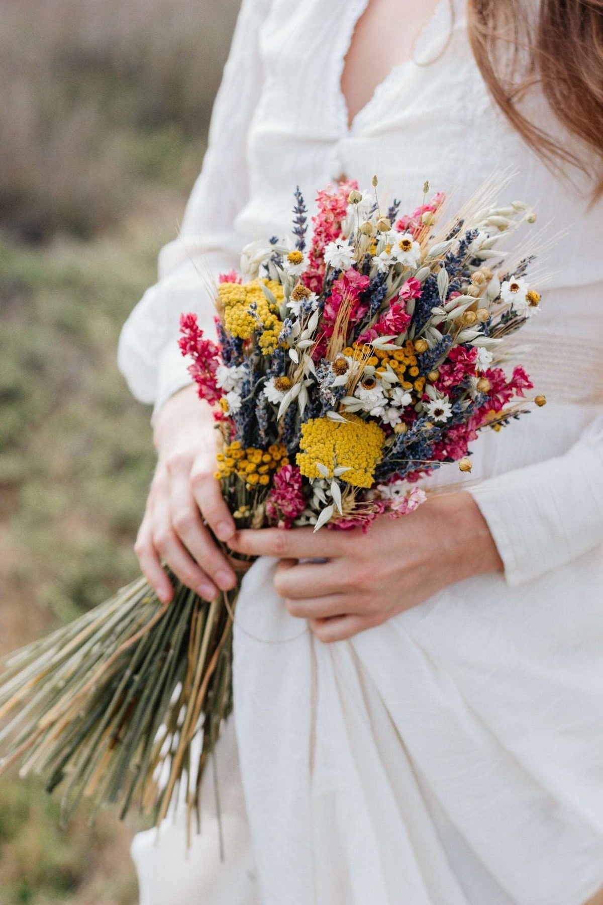Dried flower bouquet held in hands, colorful blooms with long stems and ribbon ties