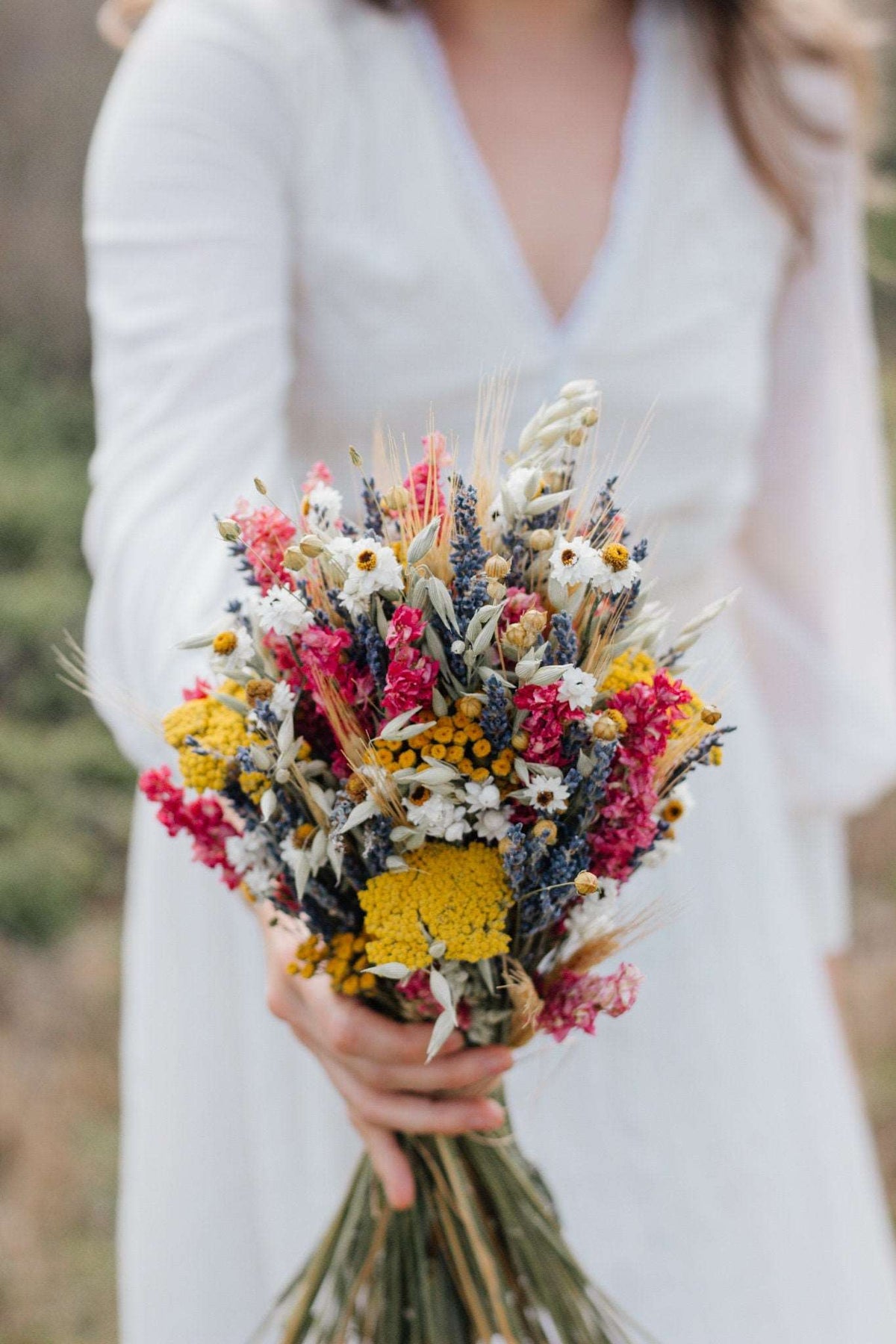 Held dried flower bouquet with bright yellow, pink, and white blooms over long stems