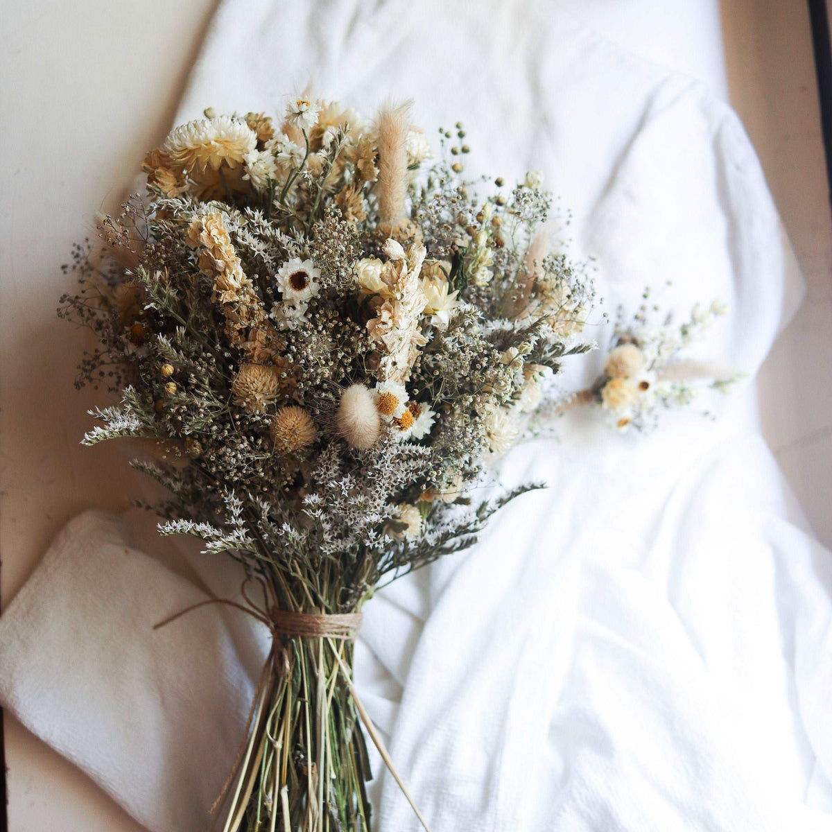 Dried flower bouquet with cream strawflower blooms and dark airy foliage bundled with twine
