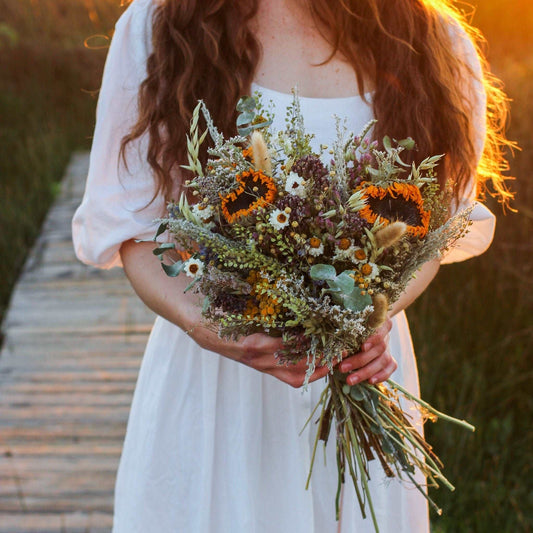Dried sunflower and eucalyptus bouquet in a rustic wrap, held by a bride