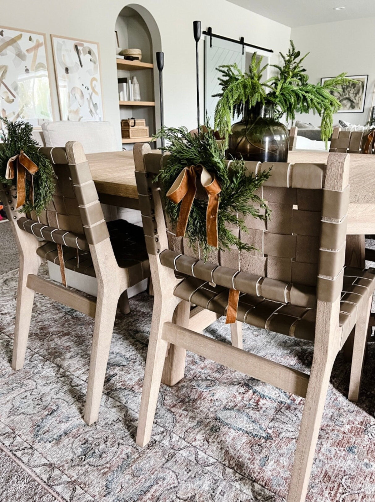Mini cedar wreath with tan ribbon bows on a dining chair back