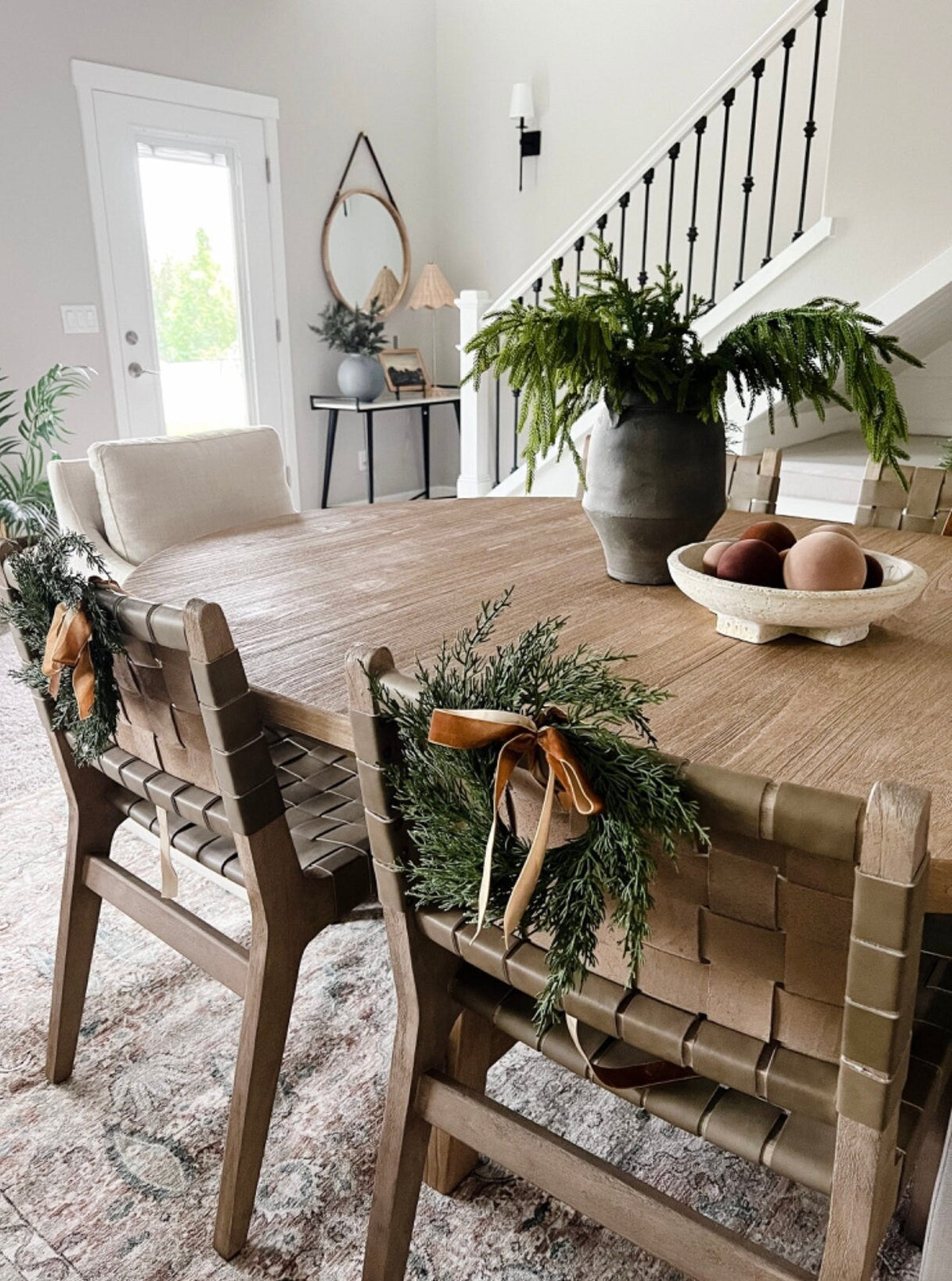 Mini cedar wreath with green foliage and tan ribbon bows on a dining table