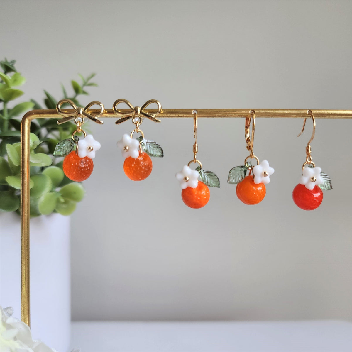Orange fruit dangle earrings with white flower charms, green leaf, gold hooks