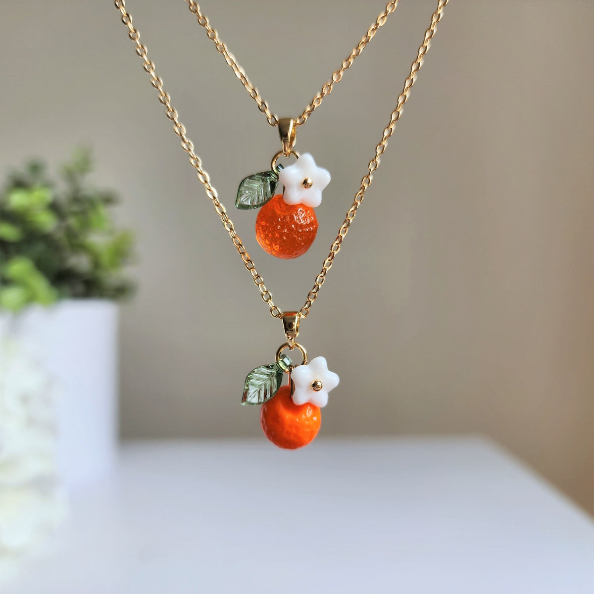 Gold-tone orange fruit charm necklace with two white flower charms and green leaves